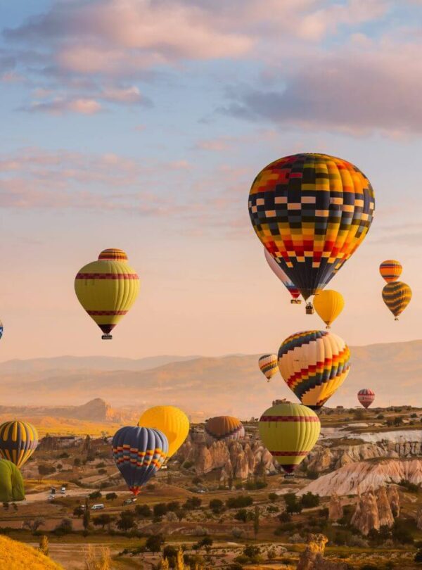 Colorful hot air balloons drifting over Cappadocia's Goreme Valley at sunrise, showcasing stunning rock formations.