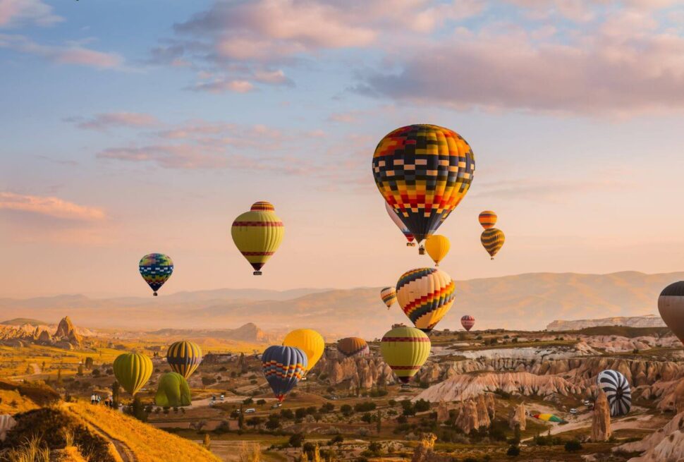 Colorful hot air balloons drifting over Cappadocia's Goreme Valley at sunrise, showcasing stunning rock formations.