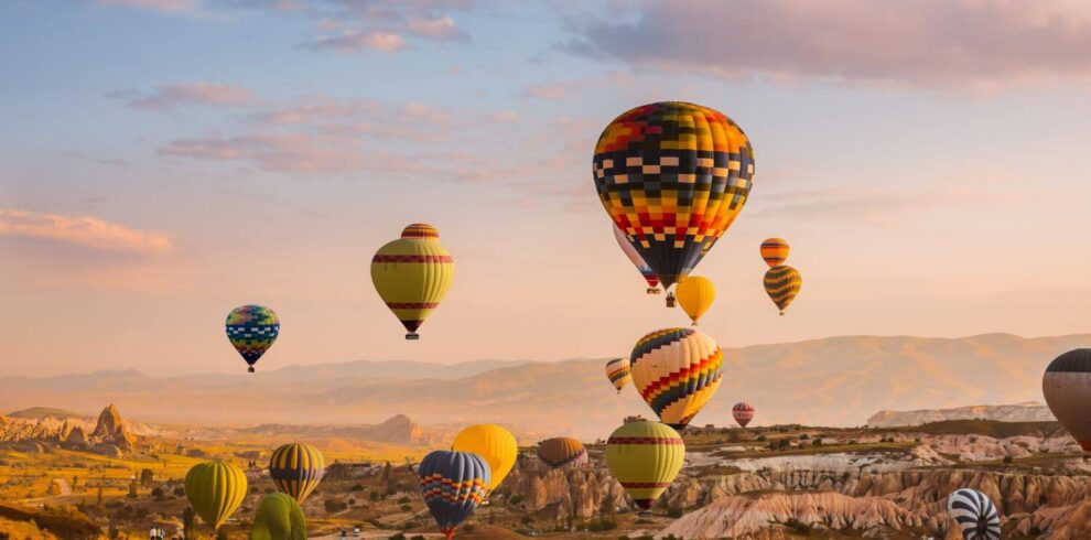 Colorful hot air balloons drifting over Cappadocia's Goreme Valley at sunrise, showcasing stunning rock formations.