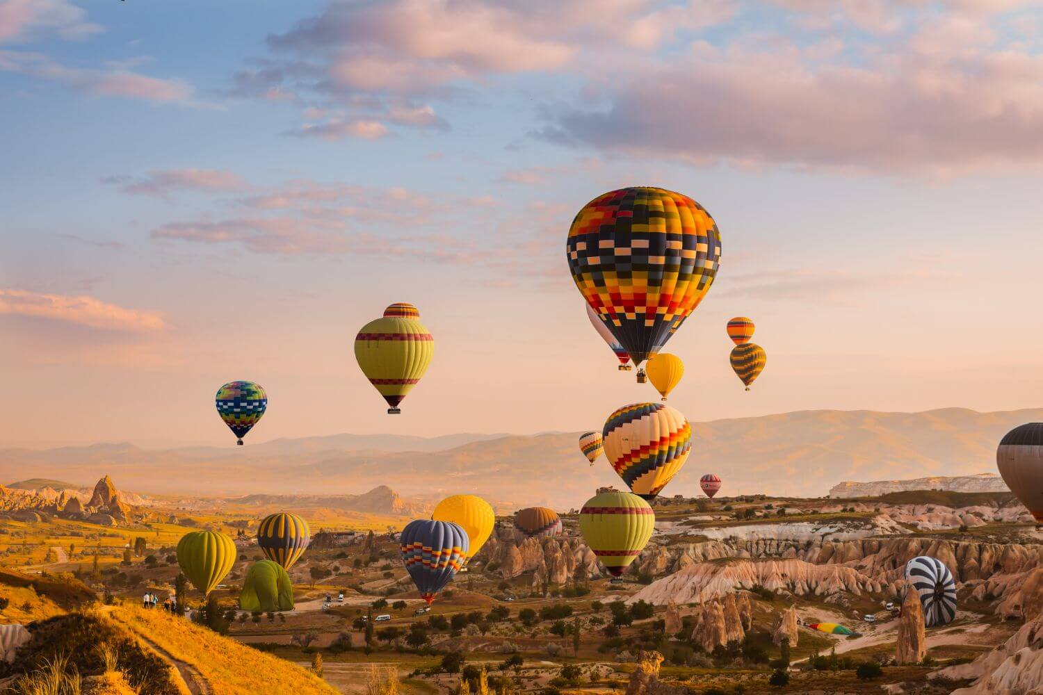 Colorful hot air balloons drifting over Cappadocia's Goreme Valley at sunrise, showcasing stunning rock formations.