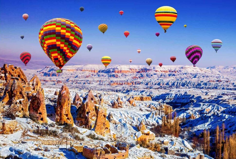 Vibrant hot air balloons soar above the snow-dusted rock formations of Cappadocia, Turkey, on a clear winter day.