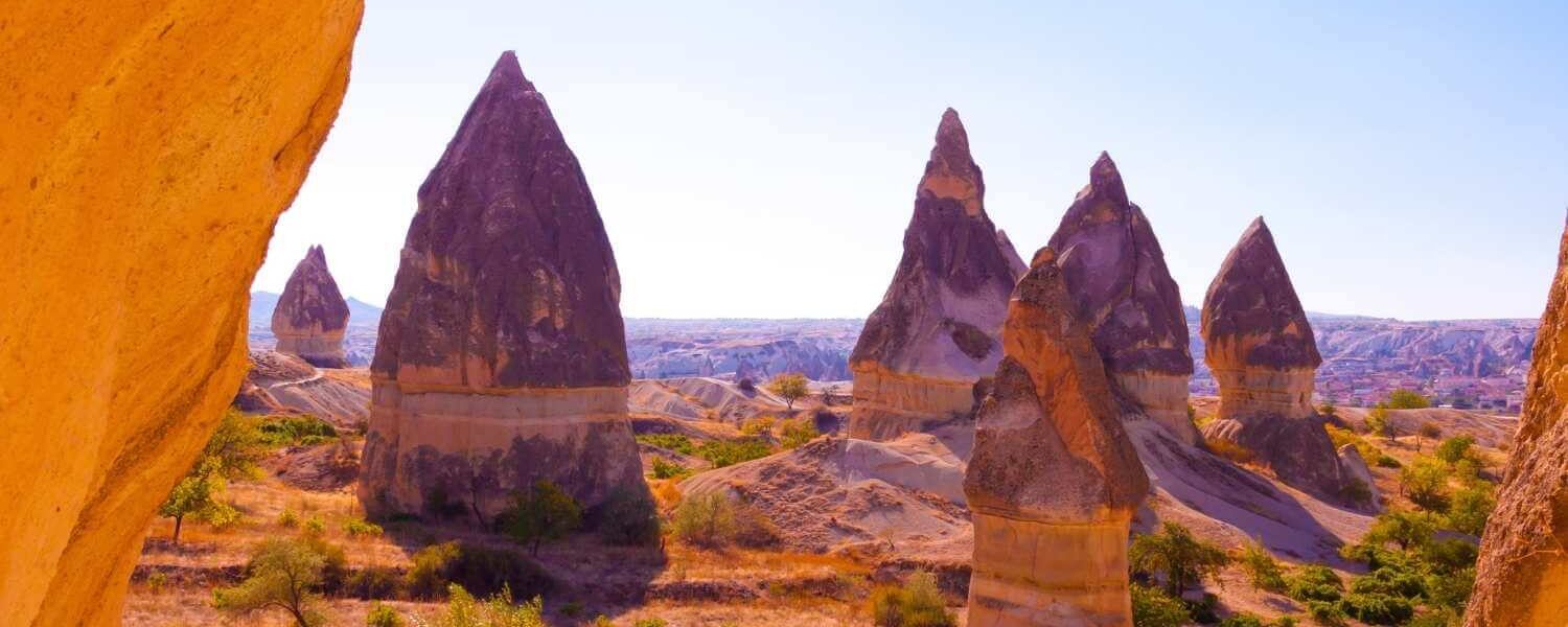 Unique conical rock formations known as fairy chimneys in Cappadocia, Turkey, under bright sunlight and a clear sky.