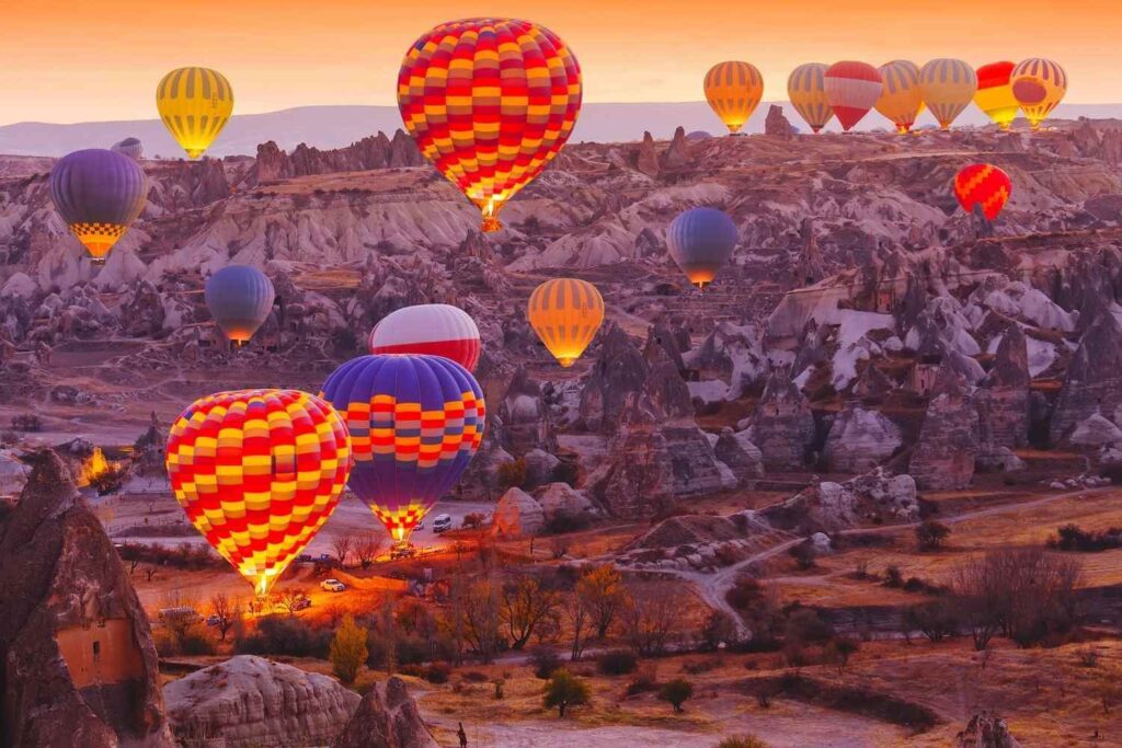 Vibrant hot air balloons float above the rocky landscape of Cappadocia, Turkey, during sunrise on a serene morning.