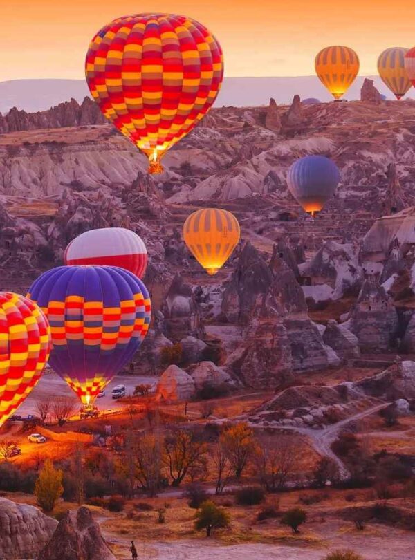 Vibrant hot air balloons float above the rocky landscape of Cappadocia, Turkey, during sunrise on a serene morning.