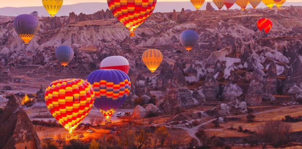 Vibrant hot air balloons float above the rocky landscape of Cappadocia, Turkey, during sunrise on a serene morning.