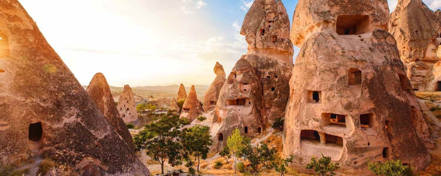 Unique rock formations with carved-out cave dwellings in Cappadocia, Turkey, under a bright sunset sky.