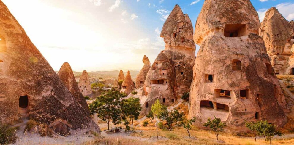 Unique rock formations with carved-out cave dwellings in Cappadocia, Turkey, under a bright sunset sky.