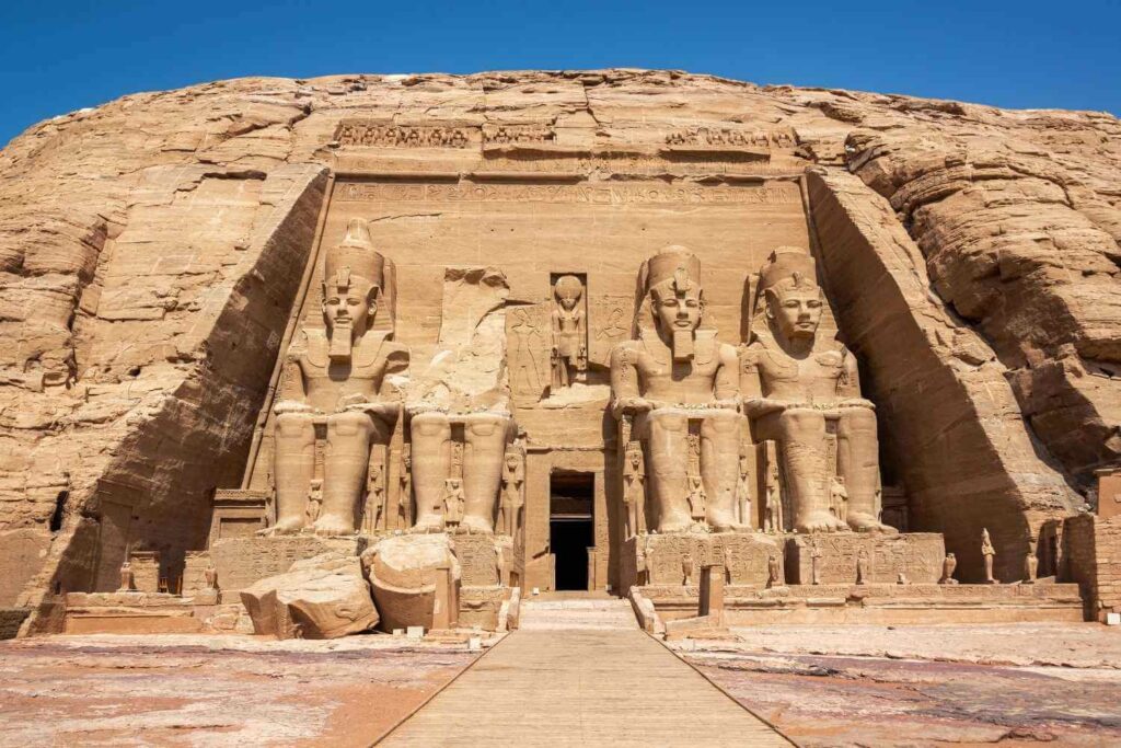 Front view of the Abu Simbel Temple in Egypt, featuring four colossal seated statues of Ramses II carved into the sandstone cliff.