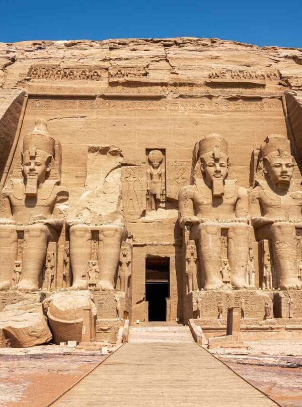 Front view of the Abu Simbel Temple in Egypt, featuring four colossal seated statues of Ramses II carved into the sandstone cliff.