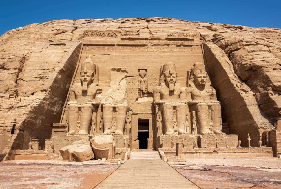 Front view of the Abu Simbel Temple in Egypt, featuring four colossal seated statues of Ramses II carved into the sandstone cliff.