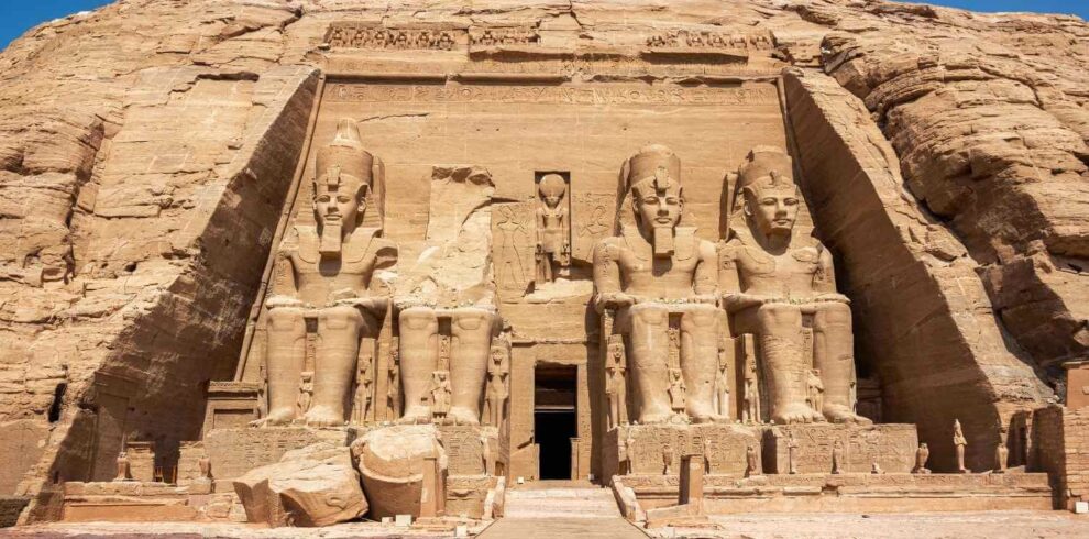 Front view of the Abu Simbel Temple in Egypt, featuring four colossal seated statues of Ramses II carved into the sandstone cliff.