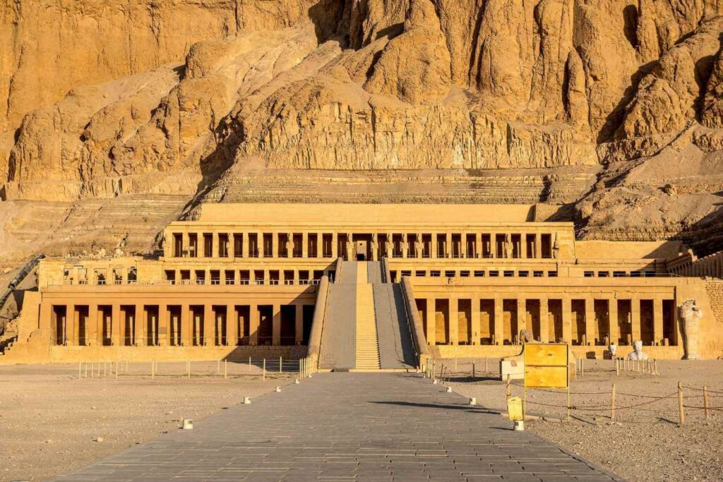 The Temple of Hatshepsut, an ancient multi-tiered structure built into a rocky cliff, illuminated by sunlight.