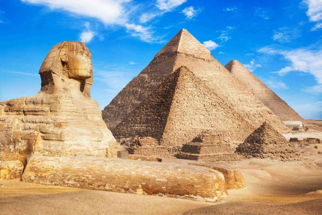 The Great Sphinx of Giza with the three large pyramids in the background, under a clear blue sky.