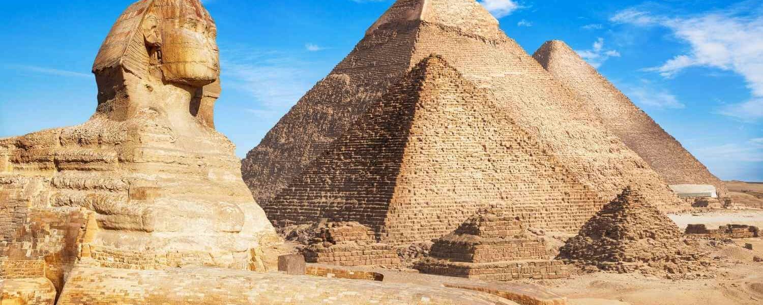 The Great Sphinx of Giza with the three large pyramids in the background, under a clear blue sky.