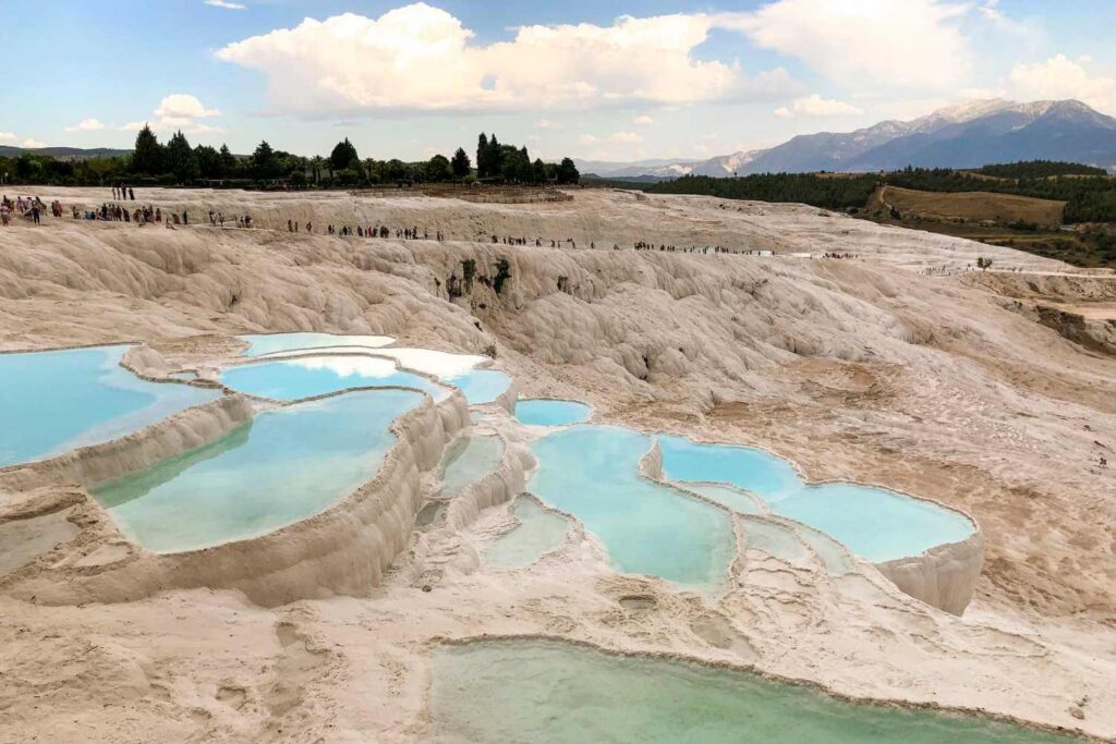 Stunning white travertine terraces of Pamukkale, Turkey, filled with turquoise thermal pools under a partly cloudy sky.