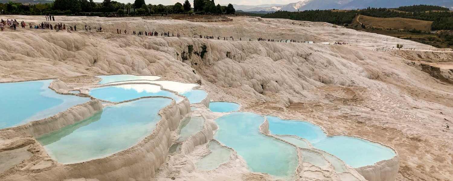 Stunning white travertine terraces of Pamukkale, Turkey, filled with turquoise thermal pools under a partly cloudy sky.