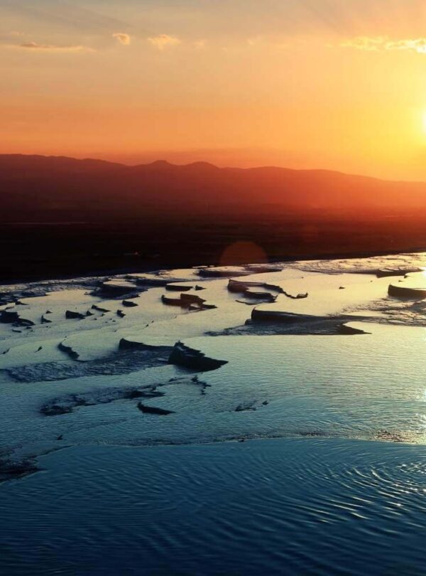 A breathtaking sunset over the thermal pools of Pamukkale, Turkey, reflecting warm orange and golden hues in the water.