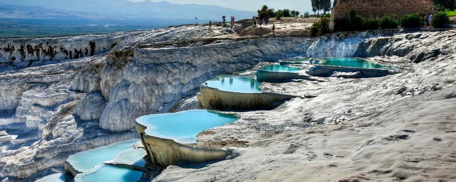 Crystal-clear turquoise pools on white travertine terraces at Pamukkale, Turkey, with tourists exploring the site.