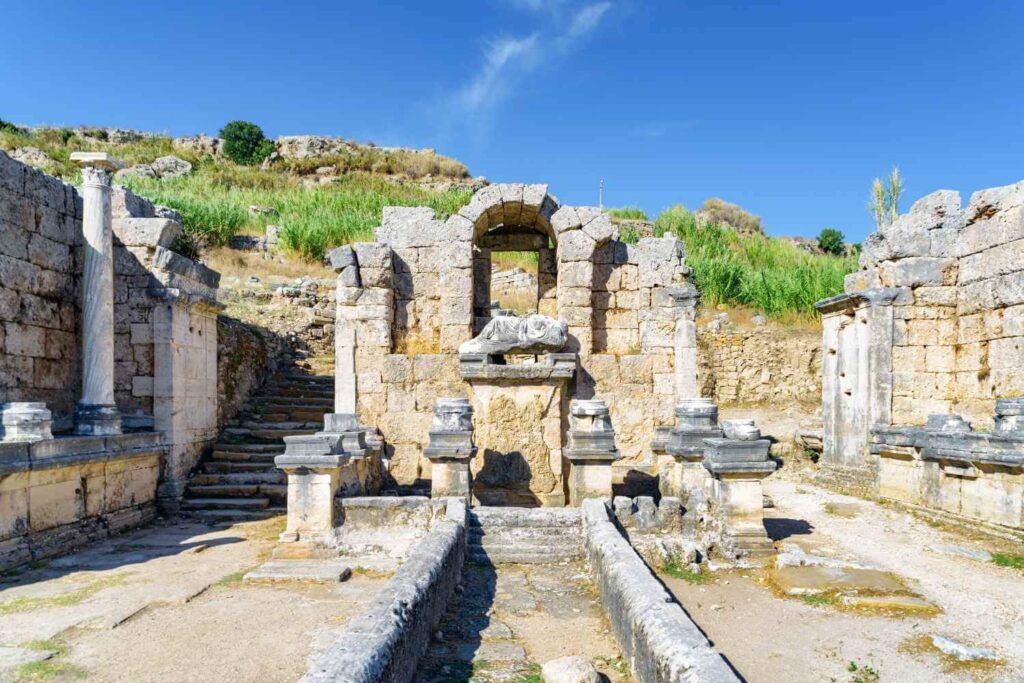 The Nymphaeum ruins in Hierapolis, featuring stone arches, columns, and weathered statues under a clear blue sky.