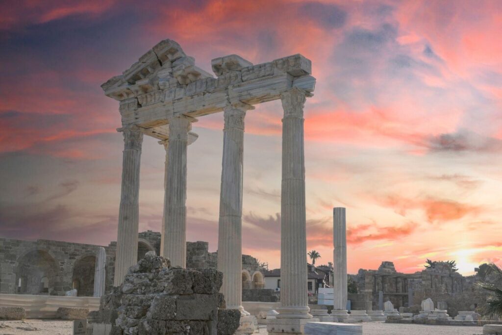 Ancient stone columns of a historic temple ruin against a vibrant sunset sky, showcasing architectural grandeur.