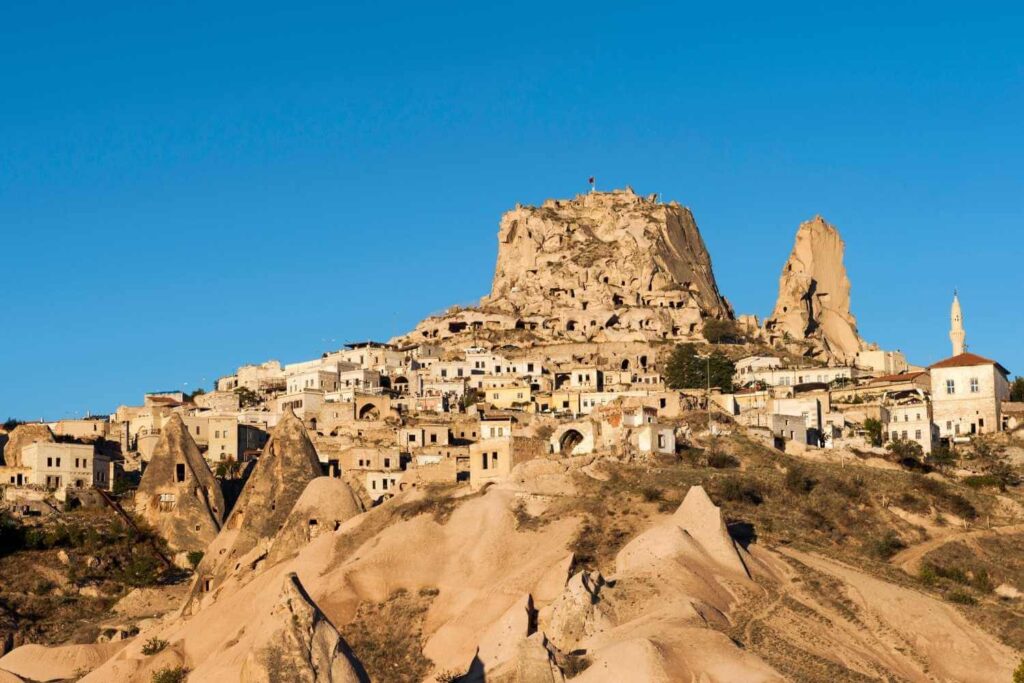 Uçhisar Castle in Cappadocia, a towering rock formation surrounded by ancient cave dwellings under a clear blue sky.