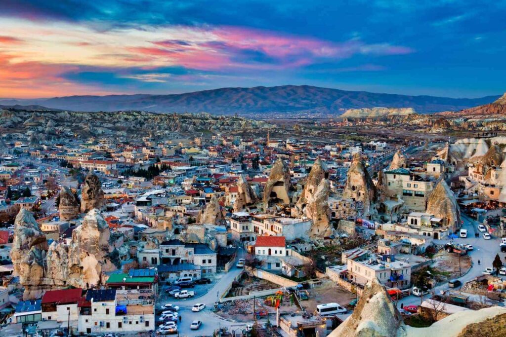 Scenic view of Cappadocia at sunset, showcasing unique rock formations, cave dwellings, and a colorful sky.