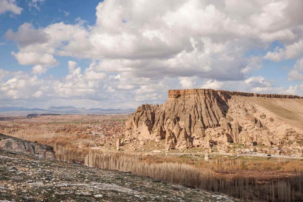 Panoramic view of Cappadocia's rugged cliffs and valley, with scattered villages under a partly cloudy sky.