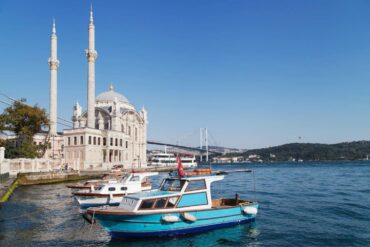 Scenic view of Ortaköy Mosque by the Bosphorus with boats in the foreground and Bosphorus Bridge in the background.