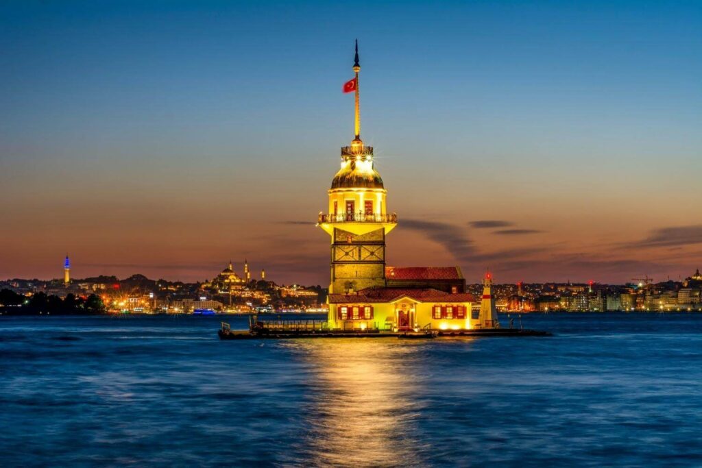 Maiden's Tower illuminated at sunset, overlooking the Bosphorus with Istanbul's cityscape in the background.