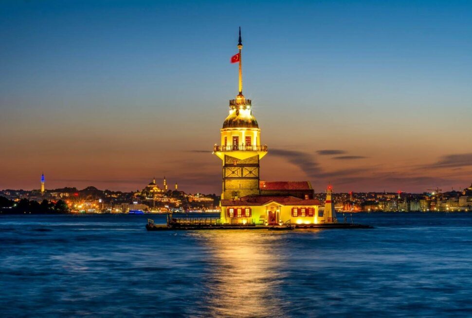 Maiden's Tower illuminated at sunset, overlooking the Bosphorus with Istanbul's cityscape in the background.