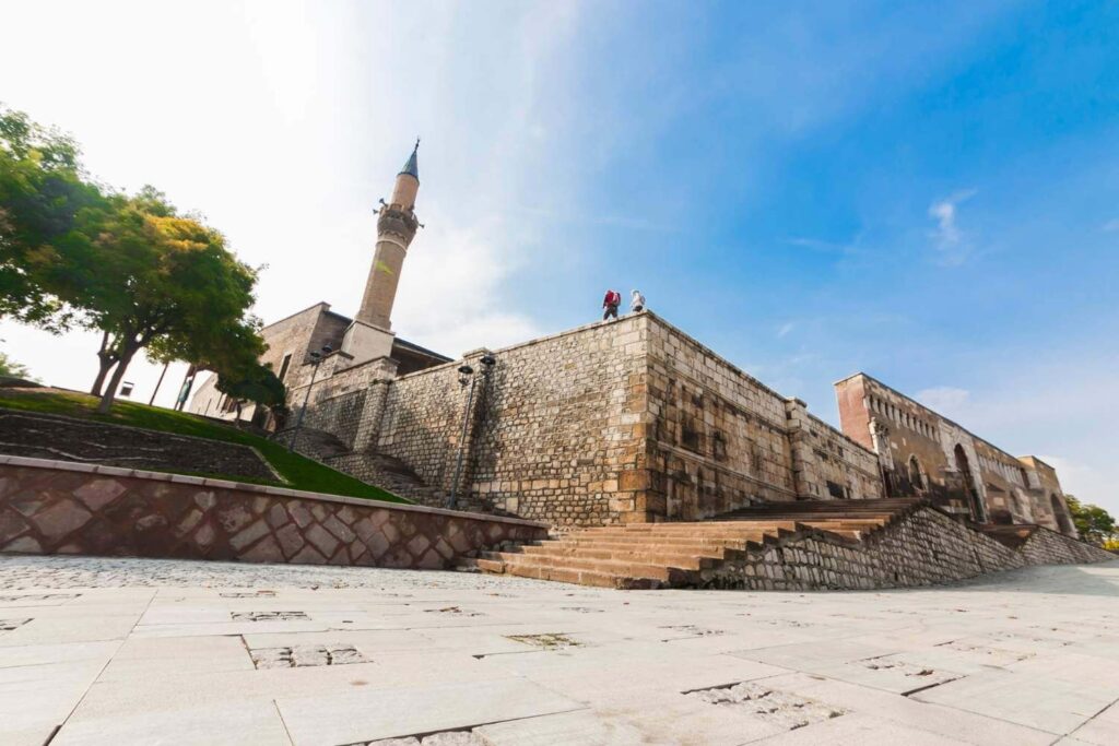 Alaaddin Mosque in Konya, Turkey, showcasing its stone architecture, tall minaret, and elevated position under a clear blue sky.