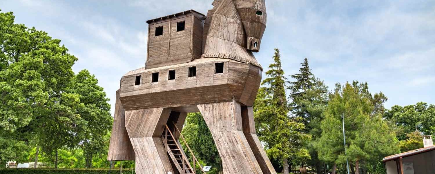 Wooden Trojan Horse replica in the ancient city of Troy, surrounded by greenery and a clear sky.