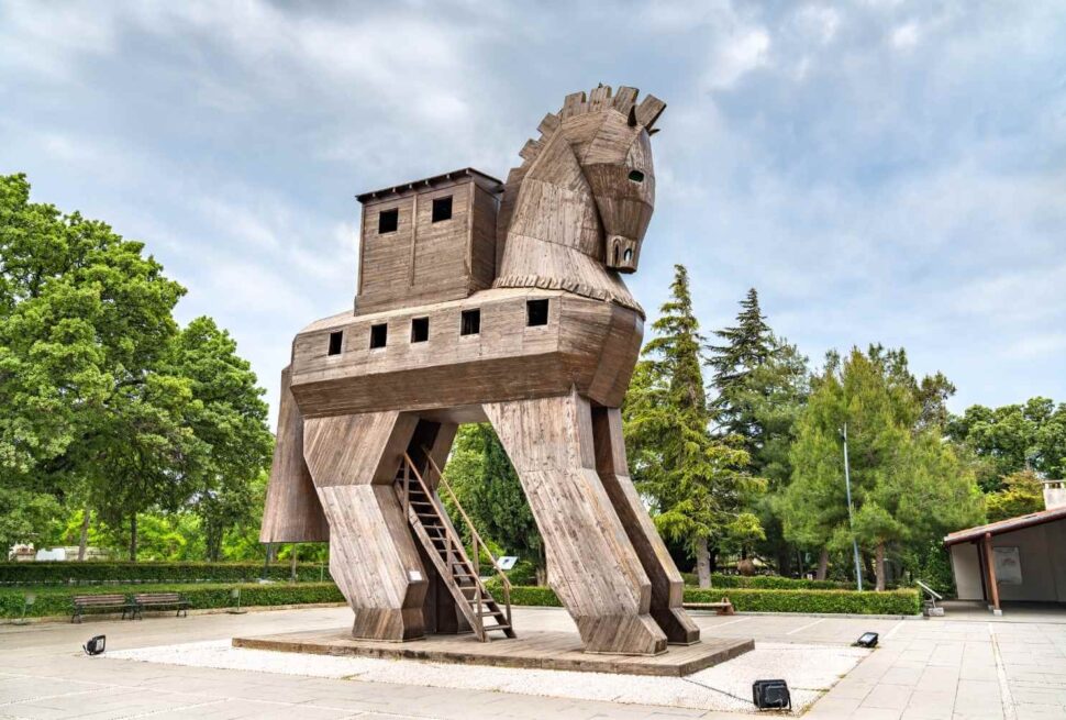 Wooden Trojan Horse replica in the ancient city of Troy, surrounded by greenery and a clear sky.